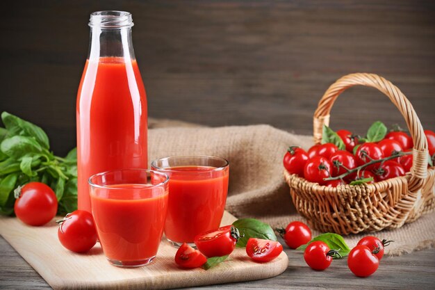 Volle fles en glazen tomatensap met groenten op houten tafel close-up