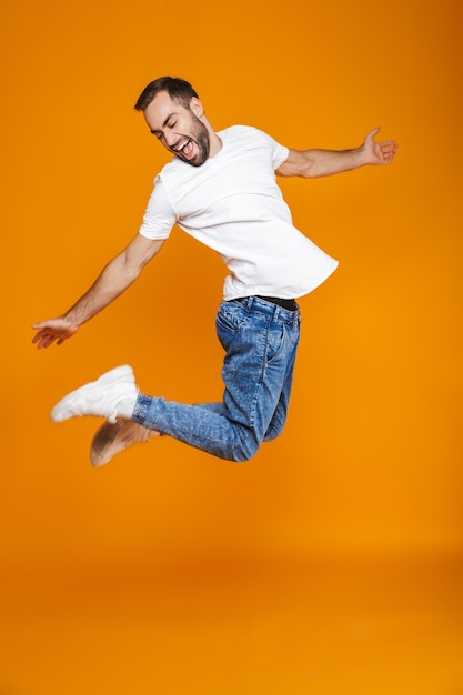 Volle lengte foto van positieve man in t-shirt en spijkerbroek springen en plezier hebben, geïsoleerd
