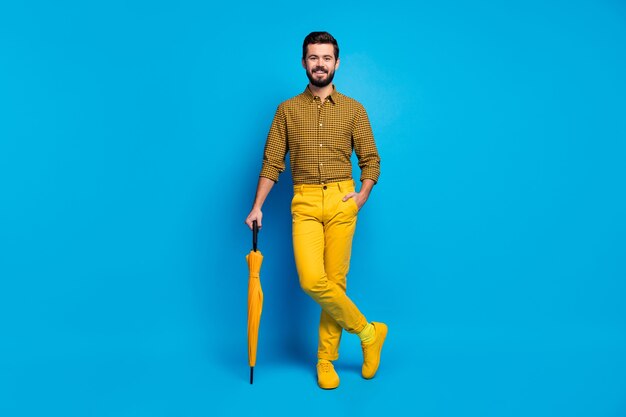 Volle lengte foto van spontane imposante man rust ontspannen hebben levendig beschermen schild regenbui parasol dragen moderne kleding schoenen geïsoleerd over blauwe kleur