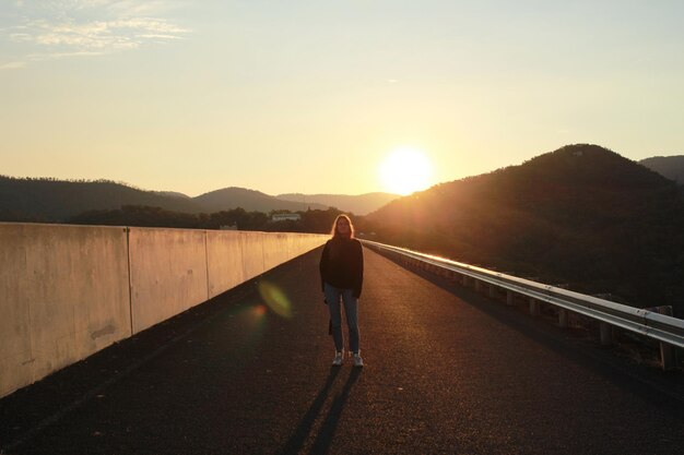 Volle lengte van een vrouw die op de weg staat tegen de hemel tijdens de zonsondergang