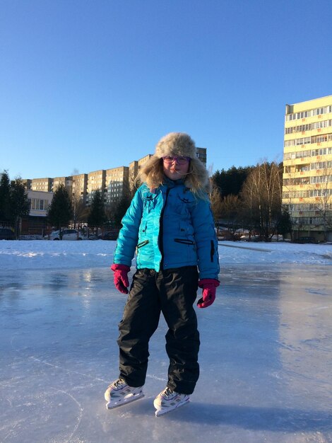 Volle lengte van meisje met warme kleding en schaatsen staande op de ijsbaan tegen de hemel tijdens de winter