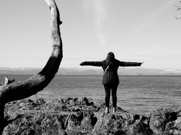Foto volle lengte van vrouw die op rots staat tegen zee en lucht.