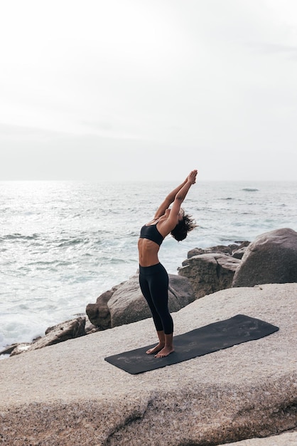 Volle lengte van vrouw die yoga doet op het strand tegen de lucht