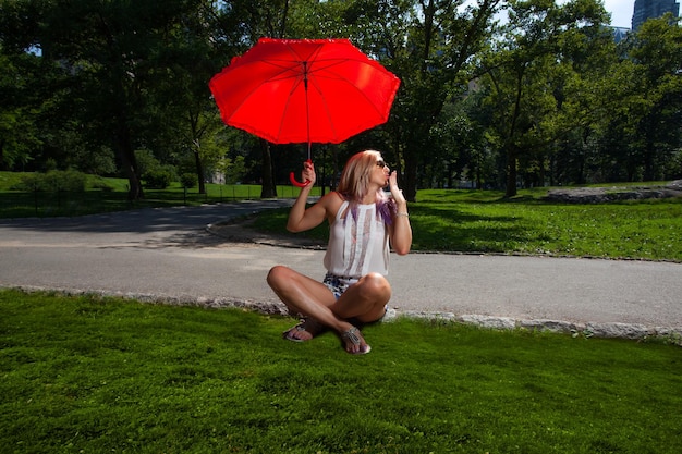 Volle lengte van vrouw met rode paraplu die in het park zit