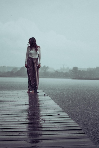 Volle lengte van vrouw staande op de pier bij het meer tegen de lucht