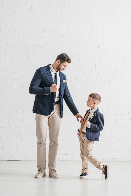 Volle lengte weergave van vader en zoon in jassen met corsages die elkaar aankijken