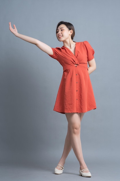 Volledig beeld van een jonge Aziatische vrouw die een oranje jurk draagt op een grijze achtergrond
