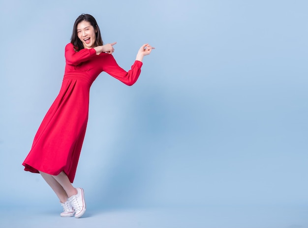 Volledig beeld van een jonge Aziatische vrouw die een rode jurk draagt op een blauwe achtergrond