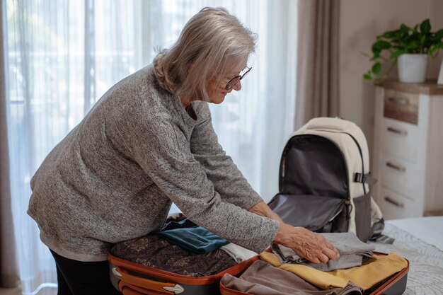 Volledig kofferconcept oudere vrouw die bagage inpakt en een rugzak voor het weekend voorbereidt