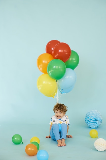 Volledig lengteportret van de vrolijke balons van de jongensholding die tegen blauwe achtergrond, het concept van de Verjaardagspartij stellen