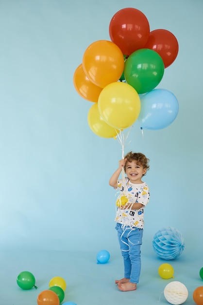 Volledig lengteportret van de vrolijke balons van de jongensholding die tegen blauwe achtergrond, het concept van de Verjaardagspartij stellen