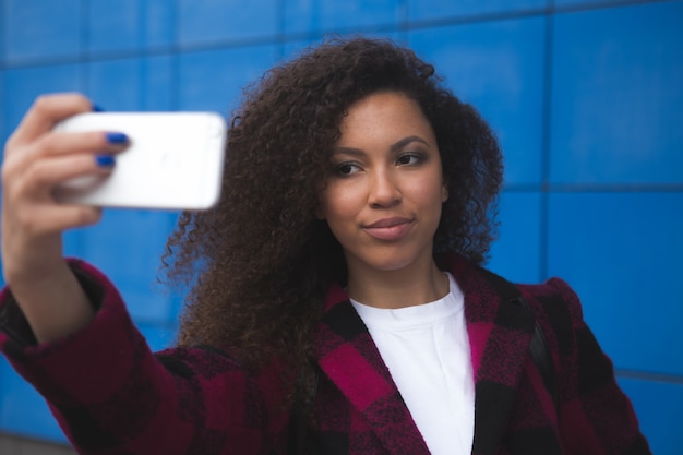 Volledig lengteportret van een glimlachende vrouw die selfie foto op smartphone maakt die op een oranje achtergrond wordt geïsoleerd