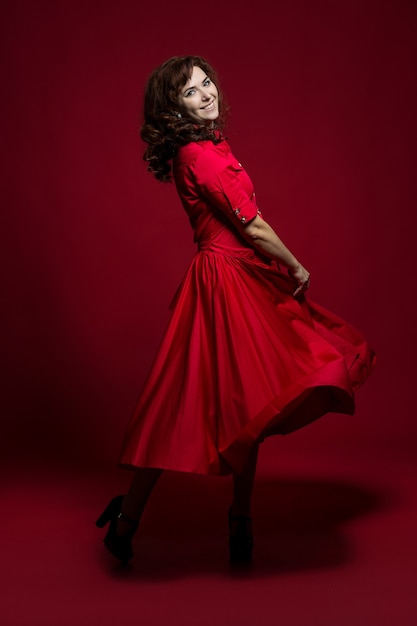 Volledig lengteportret van een roodharige vrouw in een rode jurk die zich voordeed op een rode muur