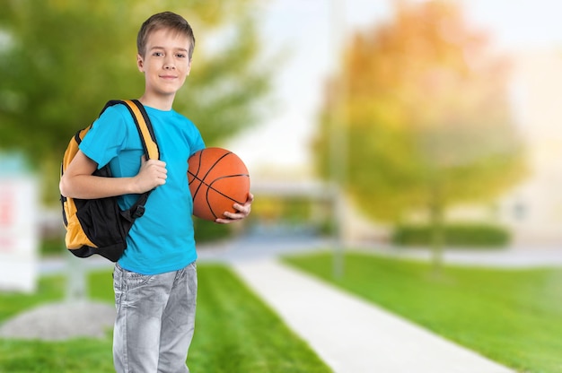 Volledig lengteportret van een schooljongen die met rugzak een basketbal houdt,