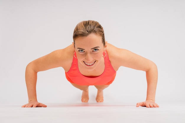 Volledig lengteportret van glimlachende jonge vrouw in sportkleding die over studioachtergrond wordt geïsoleerd