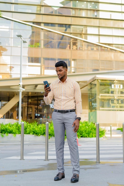 Volledig lengteportret van jonge knappe Afrikaanse zakenman in stad die telefoon verticaal schot gebruiken
