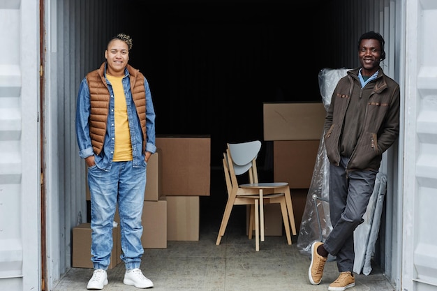 Volledig lengteportret van twee glimlachende jonge mensen die zich binnen verschepende container met dozen in bedelaars bevinden