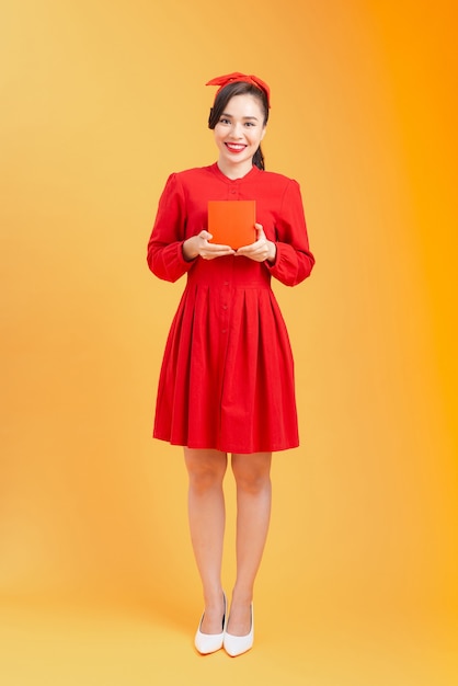 Volledig lichaamsportret van jonge Aziatische vrouw met rode giftdoos. Oranje achtergrond geïsoleerd.