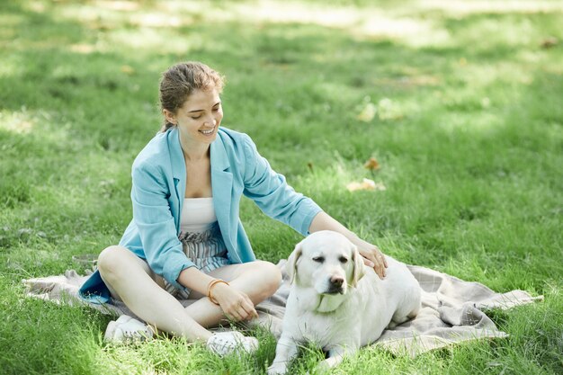 Volledig portret van een glimlachende jonge vrouw die buiten met een hond speelt terwijl ze geniet van samen wandelen in het park, kopieer ruimte