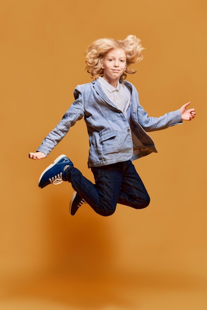 Volledig portret van een klein jongenskind in een jas die tegen een oranje studioachtergrond springt