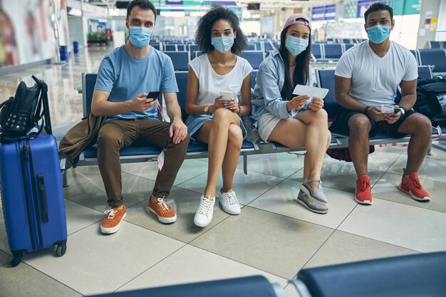 Volledig portret van een knappe groep met beschermende maskers die op de bank rusten terwijl ze wachten op een vlucht