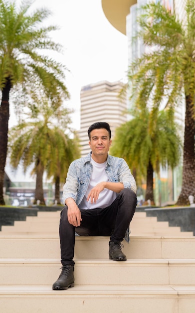 Volledig portret van een knappe jongeman die in de zomer buiten in de stad zit