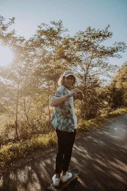 Foto volledig portret van een man die een hartvorm maakt terwijl hij over een skateboard op de weg tegen bomen staat