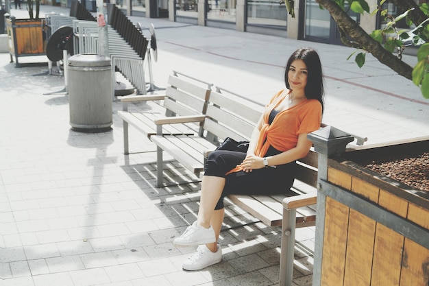 Volledig portret van een mooie vrouw die op een bankje bij de straat zit