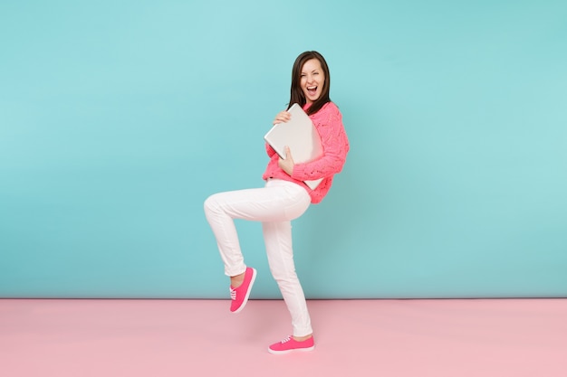 Volledig portret van een vrouw in een gebreide roze trui, witte broek met een laptop pc-computer