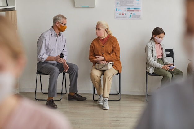 Volledig portret van senior koppel dat maskers draagt tijdens het wachten in de rij bij de kliniek of het vaccinatiecentrum, kopieer ruimte