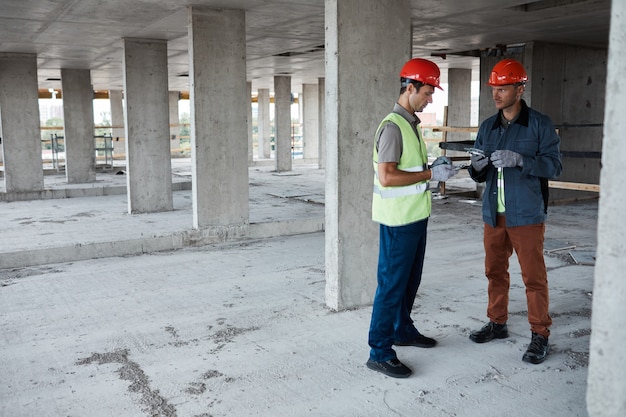 Volledig portret van twee aannemers die het project bespreken terwijl ze op de bouwplaats staan, kopieer ruimte