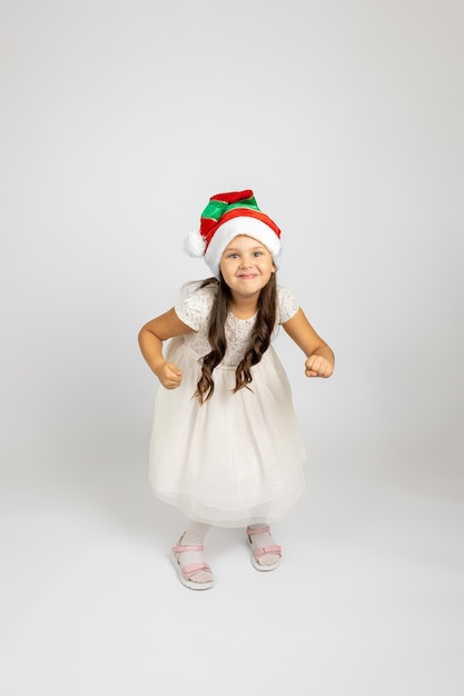 Volledig portret van vrolijk meisje in witte jurk en kerstkabouterhoed die danst en geniet van vakantie...