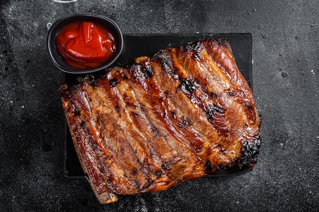 Volledig rek van BBQ-gegrilde varkensribbetjes op een marmeren bord Zwarte achtergrond Bovenaanzicht