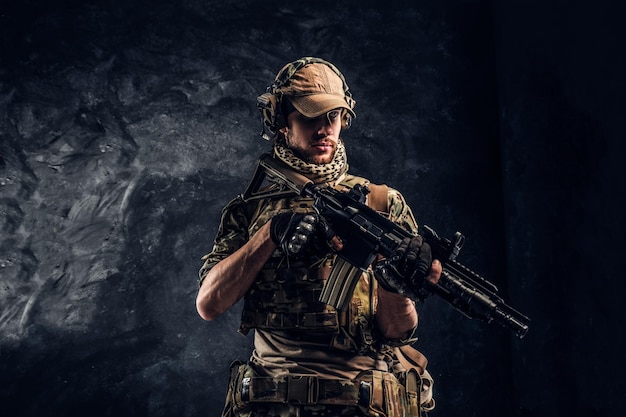 Volledig uitgeruste soldaat in camouflage-uniform met een aanvalsgeweer. studiofoto tegen een donkere getextureerde muur