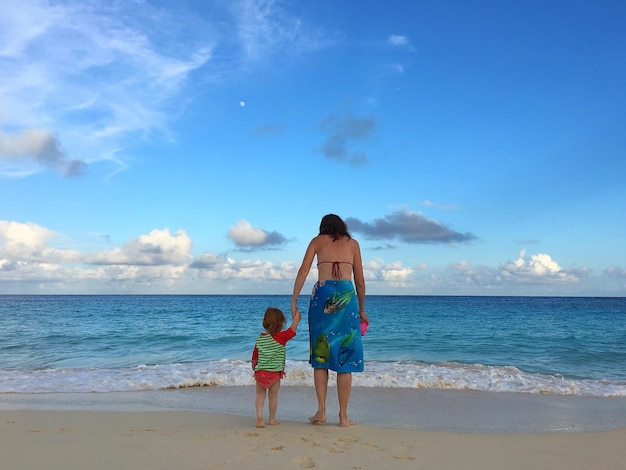Volledige achtergrondbeeld van moeder en dochter die op het strand tegen de lucht staan