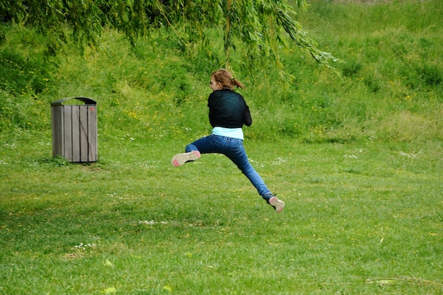 Foto volledige achterzijde van een meisje dat op een grasveld springt