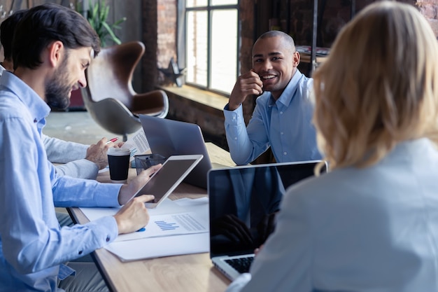 Volledige concentratie aan het werk. Groep jonge zakenmensen die werken en communiceren terwijl ze aan het bureau zitten, samen met collega's die op de achtergrond zitten.