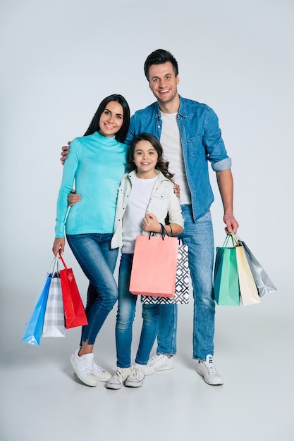 Volledige foto van een gezin dat aan het winkelen is, elkaar omhelst, met een grote glimlach in de camera kijkt en hun nieuwe aankopen in hun armen houdt.