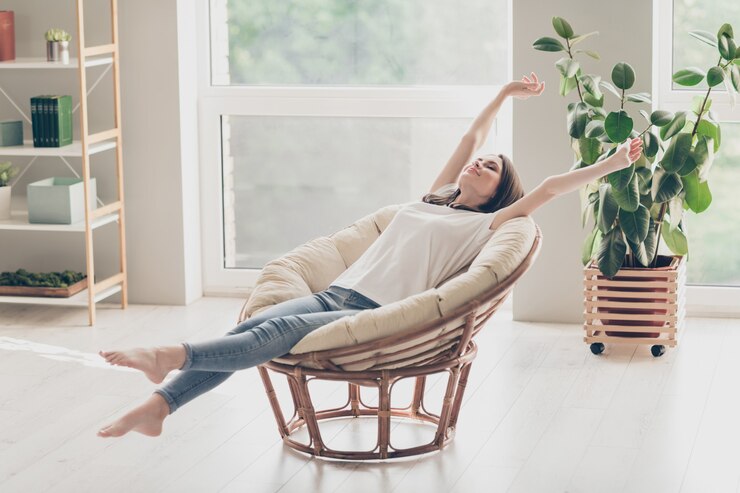 Foto volledige foto van een mooie jonge dame die in een rieten fauteuil zit, strekarmen draagt casual kleding in een appartement