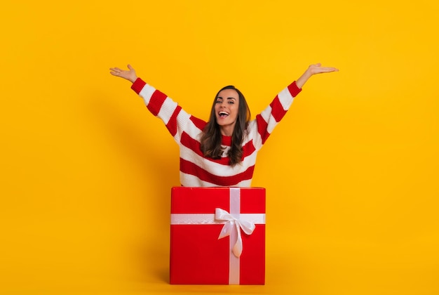 Volledige foto van een opgewonden mooie stijlvolle brunette vrouw terwijl ze zit en poseert met een grote rode geschenkdoos