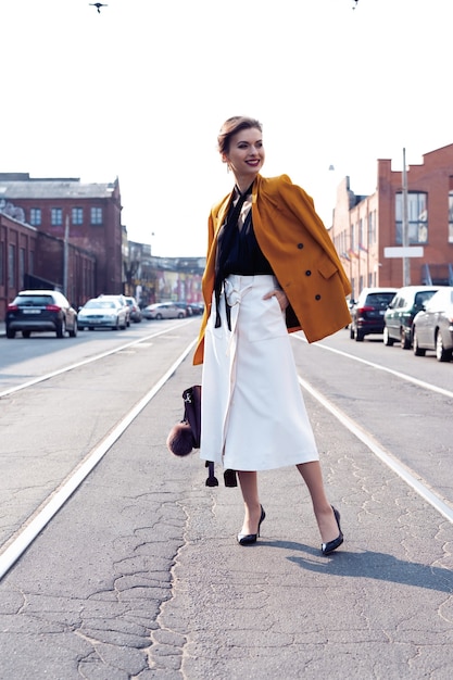Volledige foto van stijlvolle, gelukkige jonge zakenvrouw die op straat loopt