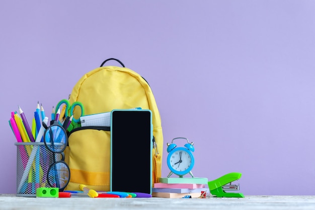 Volledige gele schoolrugzak met briefpapier op tafel op paarse achtergrond.