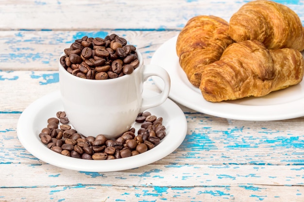 Volledige kop koffiebonen met croissants op de oude houten achtergrond. Eten en drinken concept.