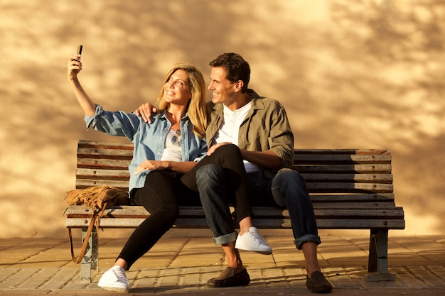 Volledige lengte gelukkige paar zittend op bankje nemen selfie