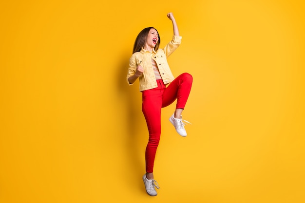 Volledige lengte lichaamsgrootte vrolijke positieve leuke aardige vrouw, gekleed in rode broek witte sneakers springen geïsoleerde levendige kleurenmuur