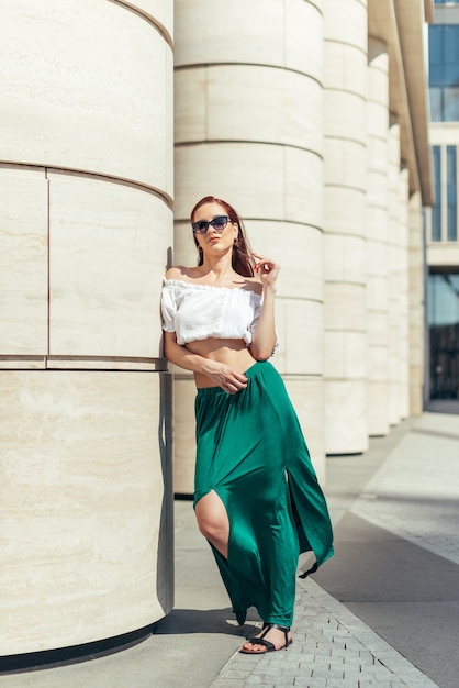 Volledige lengte meisje in zomerkleren en zonnebrillen in de buurt van een modern gebouw.