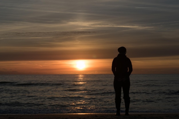 Volledige lengte van de man die op het strand staat tegen de hemel tijdens de zonsopgang