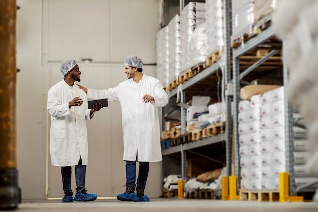 Volledige lengte van diverse voedsel fabriek opslag arbeiders bespreken en lopen naar de camera