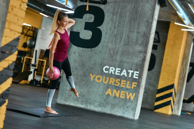 Volledige lengte van een jonge blanke vrouw in sportkleding die traint met een kleine fitnessbal op