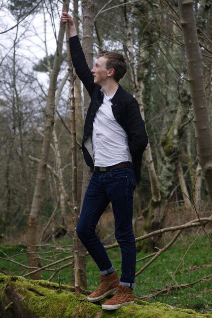 Foto volledige lengte van een man die bij een boomstam in het bos staat